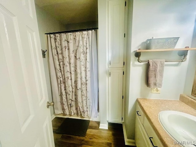 full bath with a shower with shower curtain, vanity, baseboards, and wood finished floors
