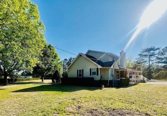 view of side of property featuring a chimney, covered porch, and a lawn