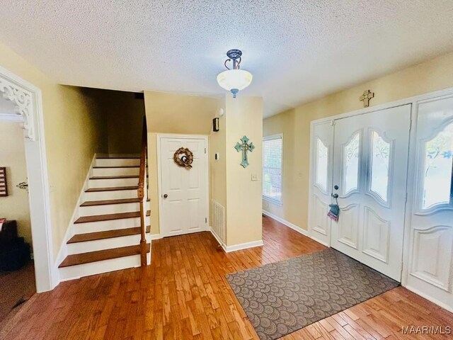 entrance foyer featuring visible vents, stairway, hardwood / wood-style flooring, and a textured ceiling