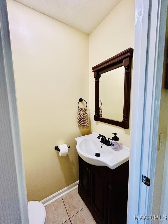 half bath with toilet, vanity, baseboards, and tile patterned flooring