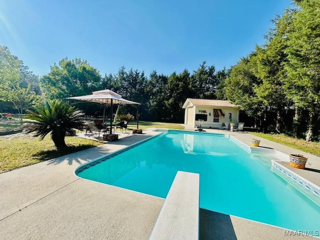 pool featuring an exterior structure, a patio, a diving board, and an outbuilding