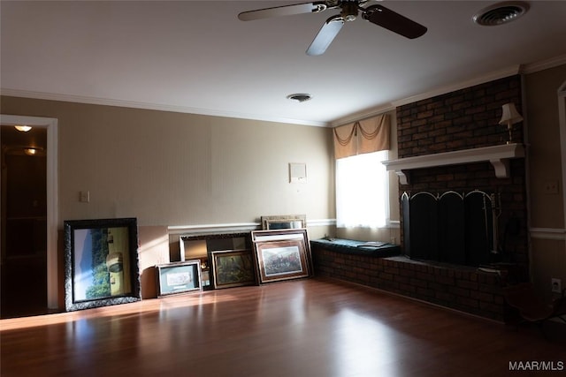 living room with a ceiling fan, visible vents, a brick fireplace, wood finished floors, and ornamental molding