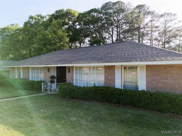 single story home featuring roof with shingles, a front yard, and brick siding