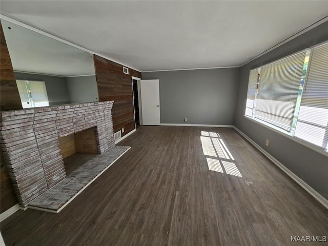 unfurnished living room with wood walls, wood finished floors, baseboards, and visible vents
