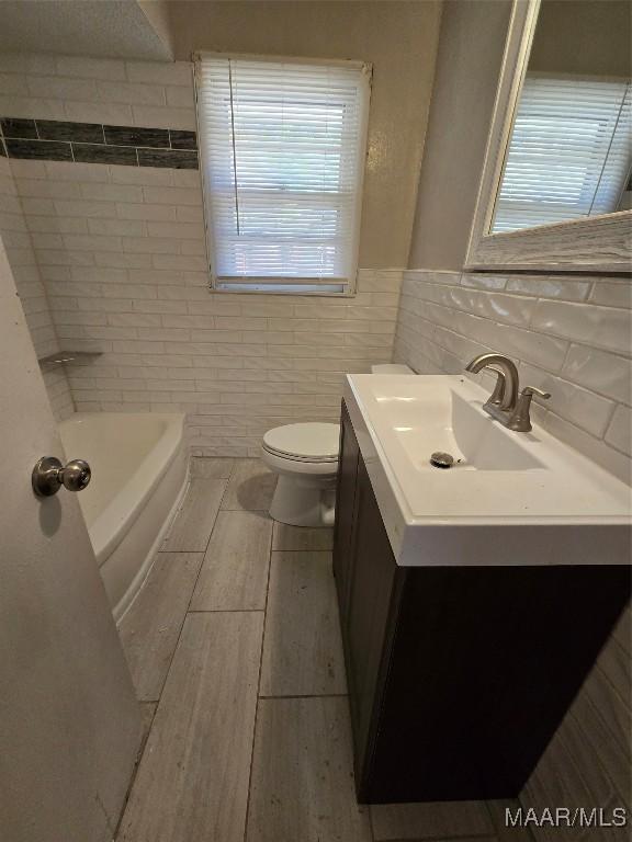 bathroom featuring tile walls, toilet, vanity, and plenty of natural light