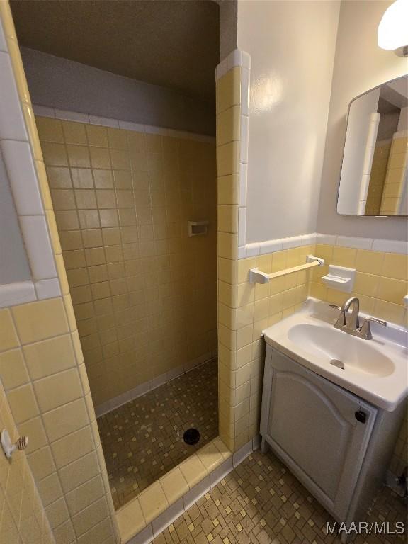 full bathroom featuring tile patterned floors, a tile shower, tile walls, wainscoting, and vanity