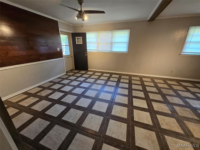 empty room with baseboards, a ceiling fan, wooden walls, and crown molding