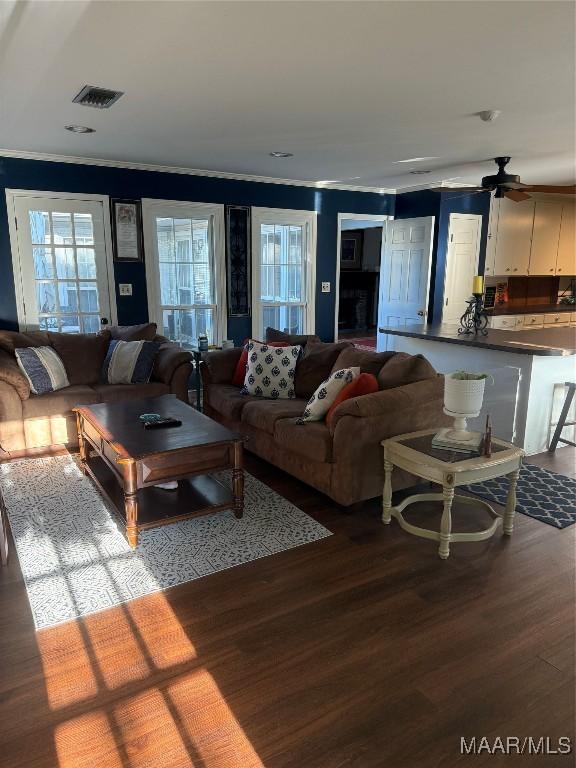 living room with ceiling fan, wood finished floors, visible vents, and ornamental molding
