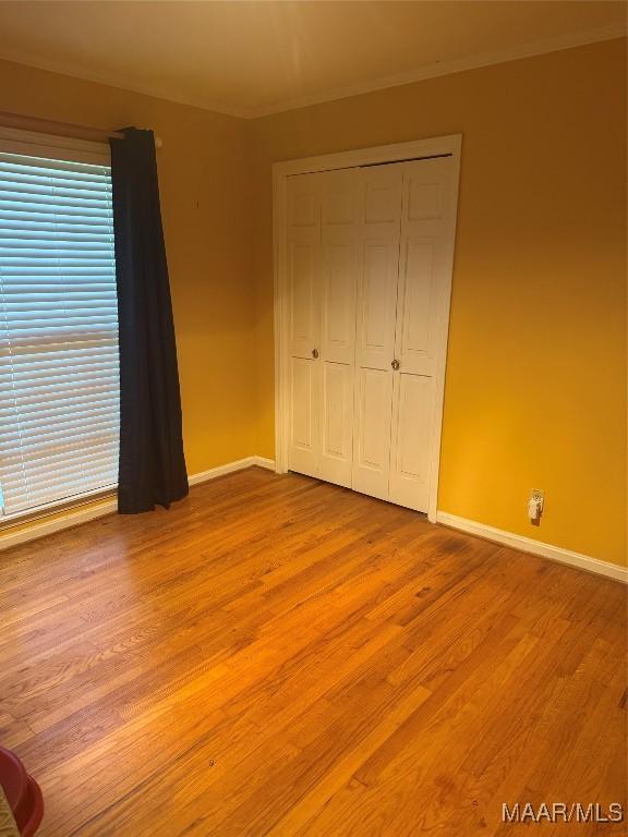 unfurnished bedroom with a closet, light wood finished floors, baseboards, and ornamental molding