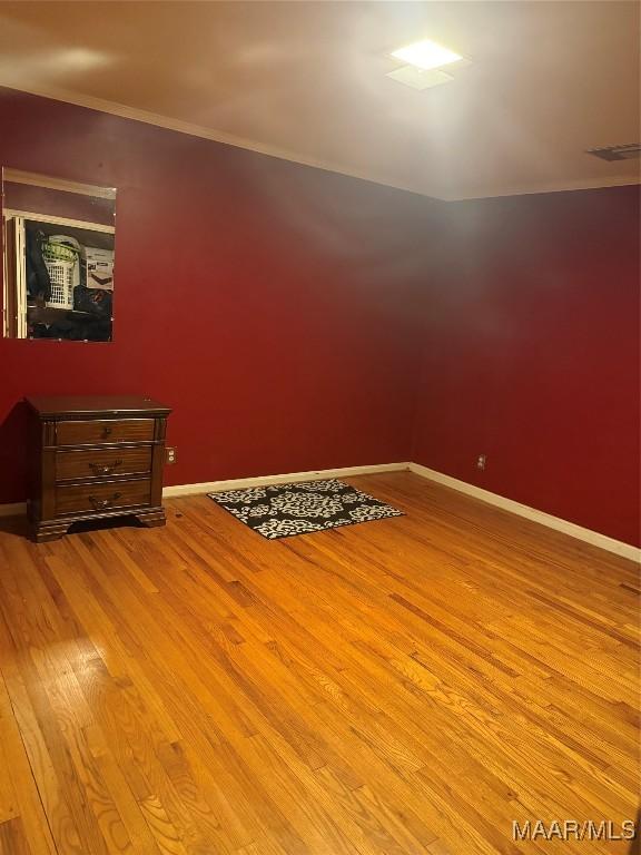 unfurnished room featuring baseboards, ornamental molding, wood finished floors, and visible vents