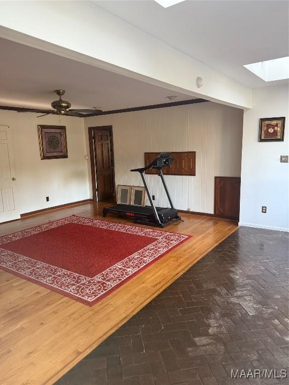 interior space featuring ceiling fan, baseboards, brick floor, and a skylight