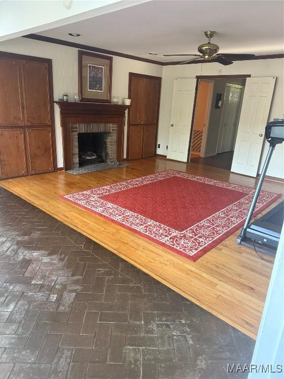 living area featuring ceiling fan, ornamental molding, a brick fireplace, and brick floor