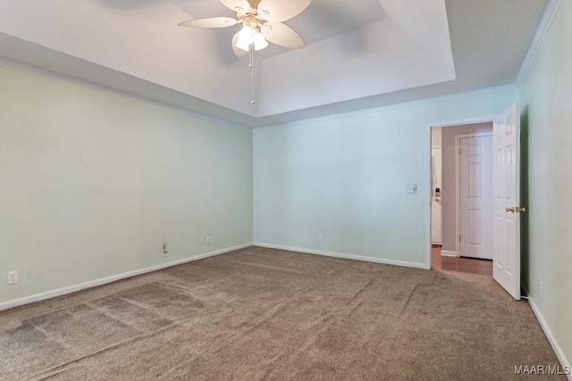 carpeted empty room with ceiling fan, baseboards, a tray ceiling, and crown molding