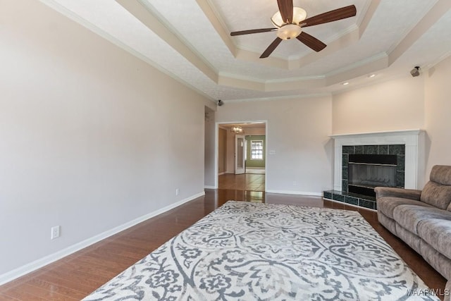 living room featuring ceiling fan, ornamental molding, a raised ceiling, a fireplace, and wood finished floors