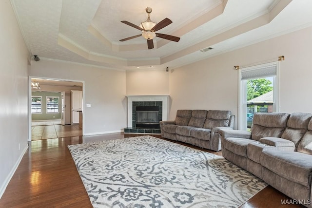 living area featuring a ceiling fan, ornamental molding, a raised ceiling, a tiled fireplace, and dark wood-style flooring