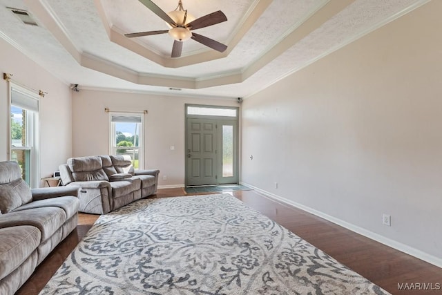 living area with ornamental molding, ceiling fan, dark wood-style floors, a tray ceiling, and baseboards