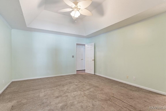 carpeted empty room featuring a tray ceiling, ceiling fan, baseboards, and crown molding