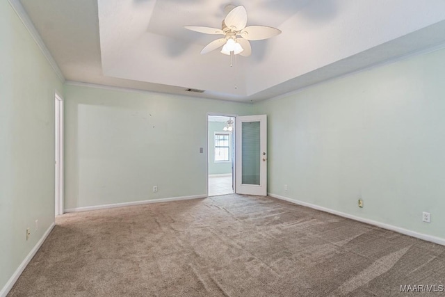 spare room featuring a raised ceiling, carpet floors, a ceiling fan, baseboards, and ornamental molding