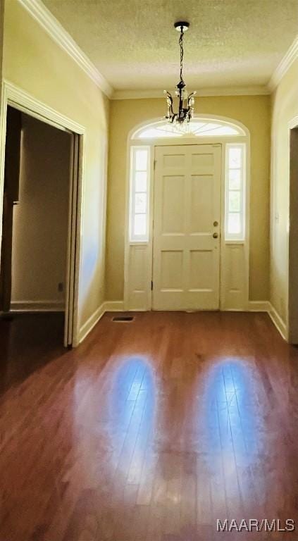 foyer entrance with a textured ceiling, baseboards, a notable chandelier, wood finished floors, and crown molding