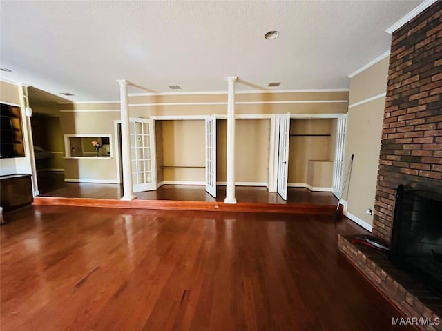 unfurnished living room featuring baseboards, wood finished floors, ornate columns, and ornamental molding