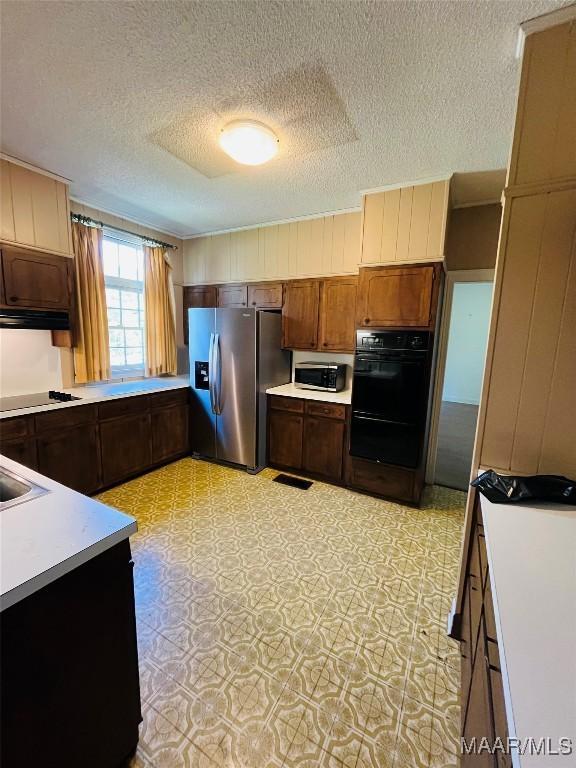 kitchen featuring ventilation hood, a sink, a textured ceiling, light countertops, and black appliances