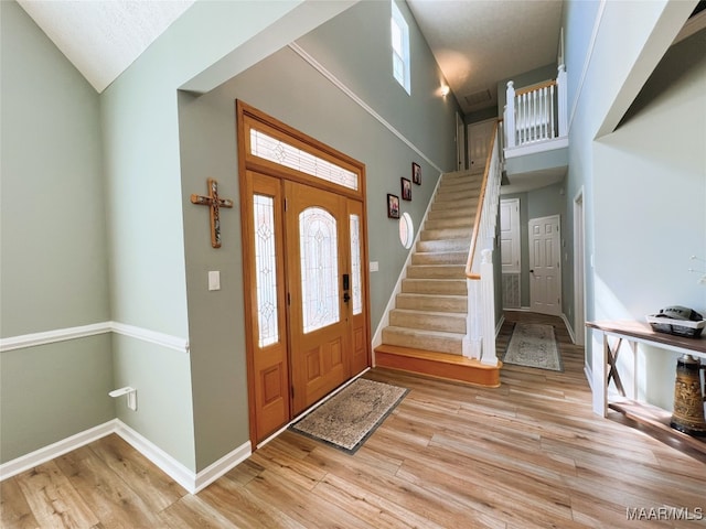 entrance foyer with baseboards, stairway, high vaulted ceiling, and light wood-type flooring