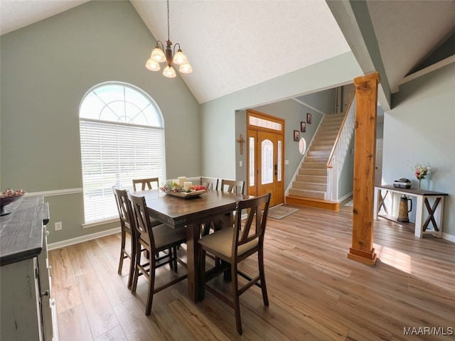 dining area with high vaulted ceiling, stairs, light wood finished floors, baseboards, and a notable chandelier
