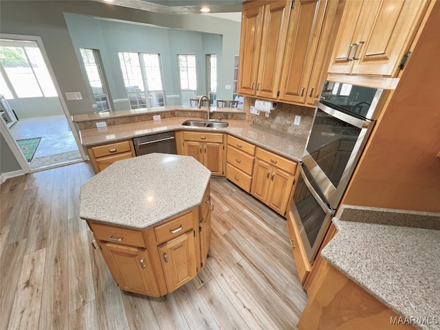 kitchen with light stone counters, a sink, light wood-style floors, dishwasher, and a kitchen island