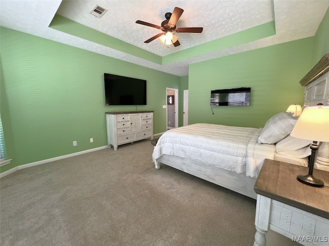 carpeted bedroom featuring a ceiling fan, a textured ceiling, a tray ceiling, baseboards, and visible vents