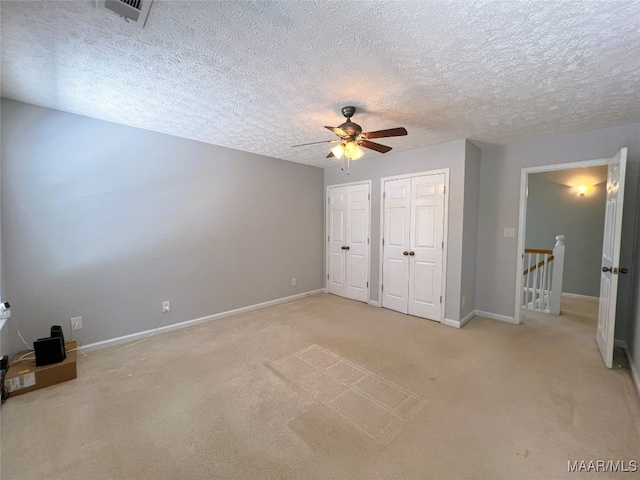 unfurnished bedroom with a textured ceiling, multiple closets, light colored carpet, baseboards, and visible vents