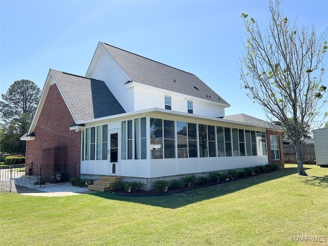 back of property featuring a yard, a sunroom, a shingled roof, and fence