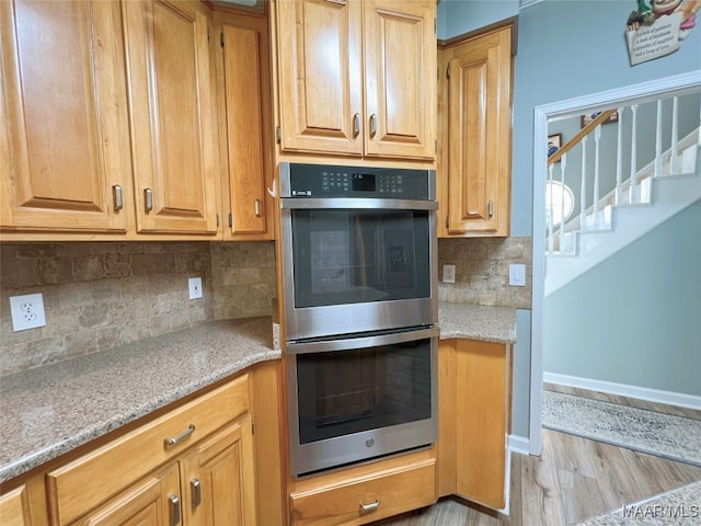 kitchen featuring stainless steel double oven, light stone counters, light wood-type flooring, baseboards, and tasteful backsplash