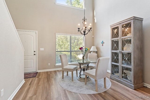 dining room featuring baseboards, wood finished floors, a high ceiling, and a chandelier