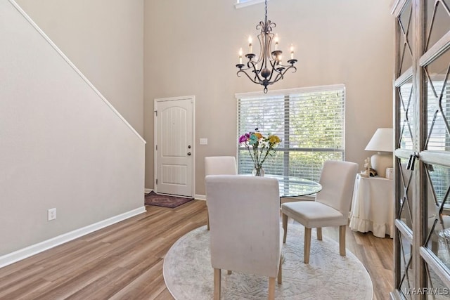 dining space featuring baseboards, an inviting chandelier, a towering ceiling, and light wood-style flooring