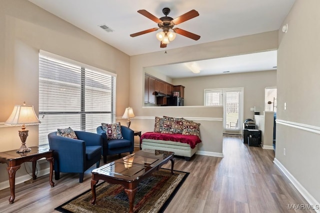 living area with visible vents, baseboards, wood finished floors, and ceiling fan