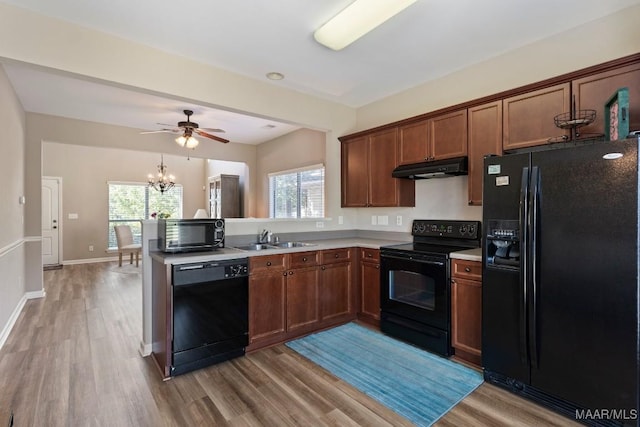 kitchen with under cabinet range hood, light countertops, a sink, light wood-type flooring, and black appliances
