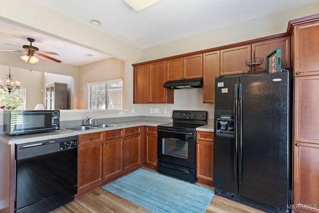 kitchen featuring light wood-type flooring, under cabinet range hood, a sink, and black appliances