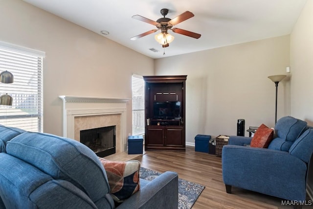 living area with a high end fireplace, wood finished floors, visible vents, baseboards, and ceiling fan