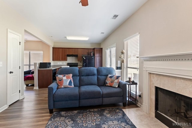 living room featuring a tiled fireplace, visible vents, light wood finished floors, and baseboards