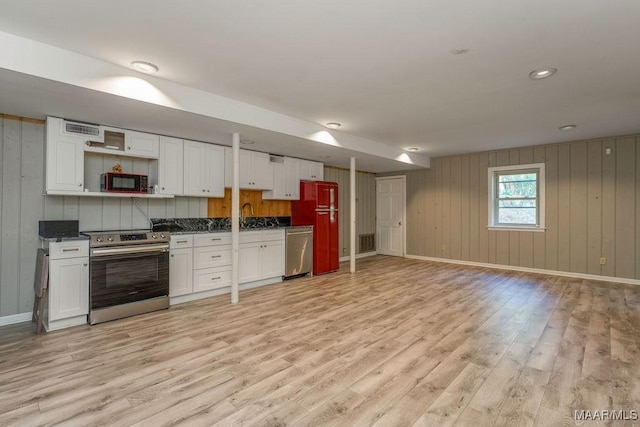 kitchen featuring appliances with stainless steel finishes, light wood finished floors, dark countertops, white cabinetry, and wooden walls