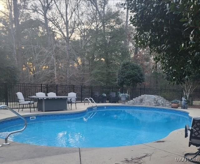 view of swimming pool with fence, a patio area, and view of scattered trees