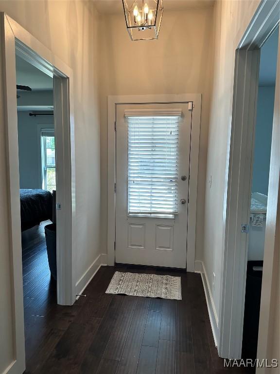 doorway to outside featuring dark wood-style flooring, a notable chandelier, and baseboards