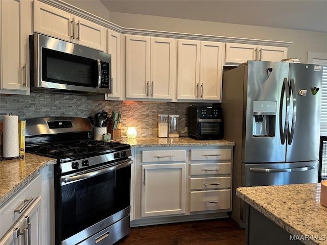kitchen with appliances with stainless steel finishes, white cabinetry, light stone countertops, and backsplash