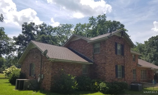view of side of home with brick siding, a yard, roof with shingles, and central AC