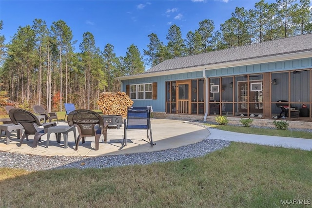 rear view of house with board and batten siding, a patio area, a lawn, and a sunroom
