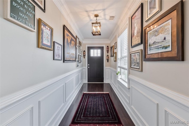 doorway with a decorative wall, a wainscoted wall, ornamental molding, dark wood-type flooring, and visible vents