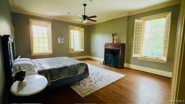 bedroom featuring wood finished floors, baseboards, a fireplace, and ceiling fan