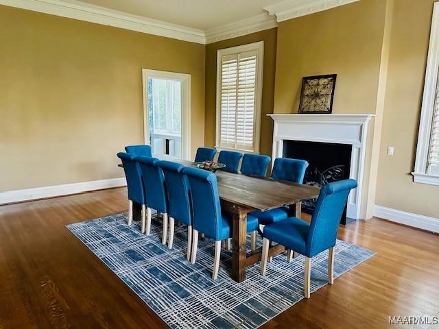 dining space featuring wood finished floors, baseboards, a fireplace, and crown molding