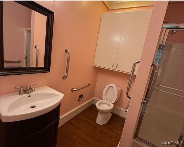 bathroom with toilet, wood finished floors, a stall shower, vanity, and baseboards