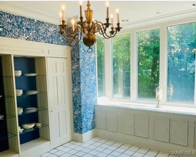 unfurnished dining area featuring wallpapered walls, ornamental molding, light tile patterned flooring, baseboards, and a notable chandelier